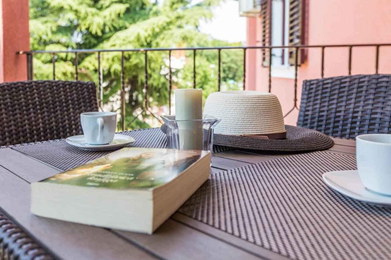 A table with a book, a candle, and a cup on a balcony with wicker chairs and a railing.