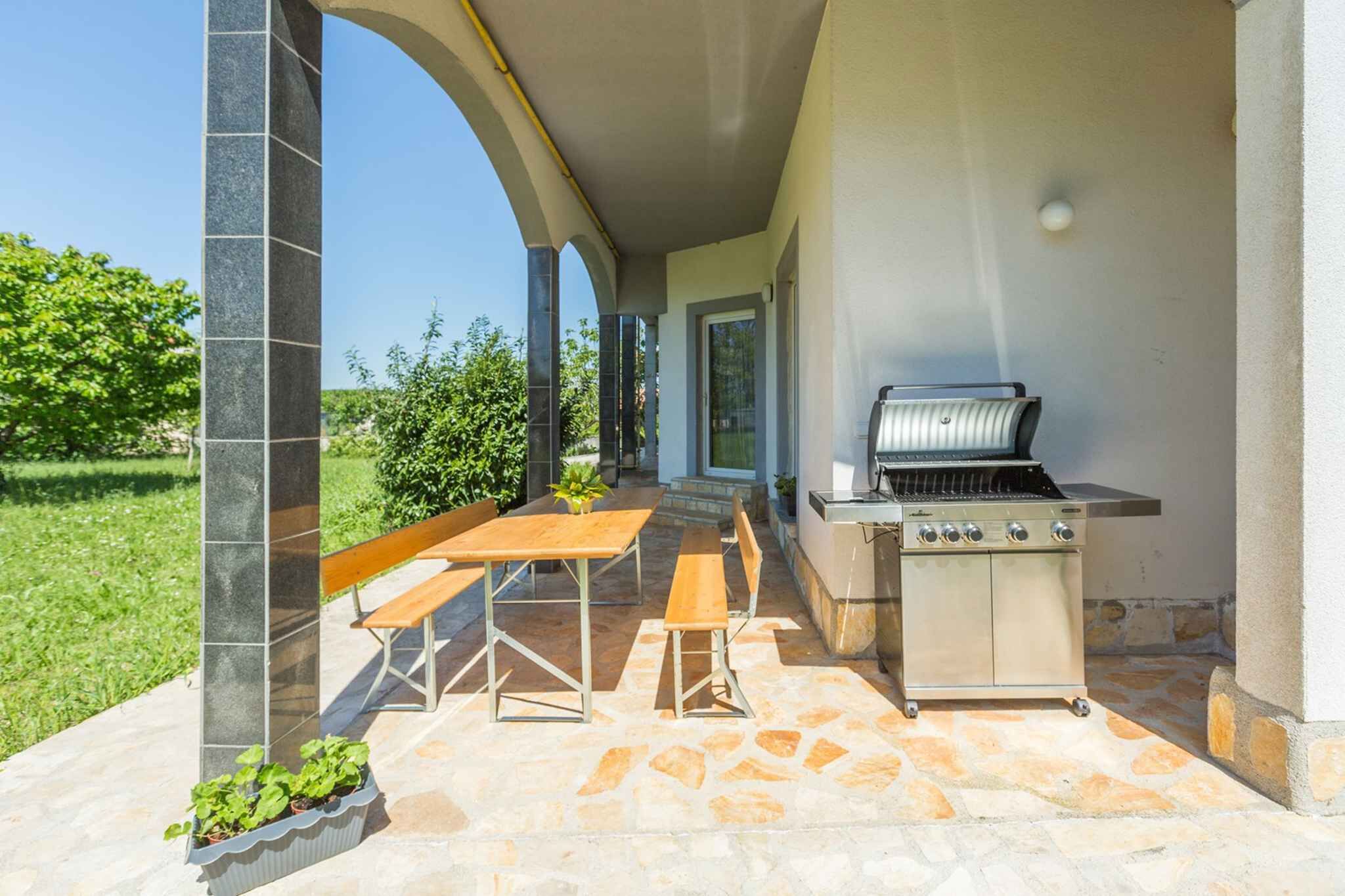Patio esterno con barbecue, pavimento in pietra e panche di legno.
