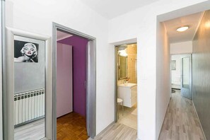 Un pasillo con un radiador, un baño con lavamanos y espejo, y una puerta con un cuadro enmarcado.