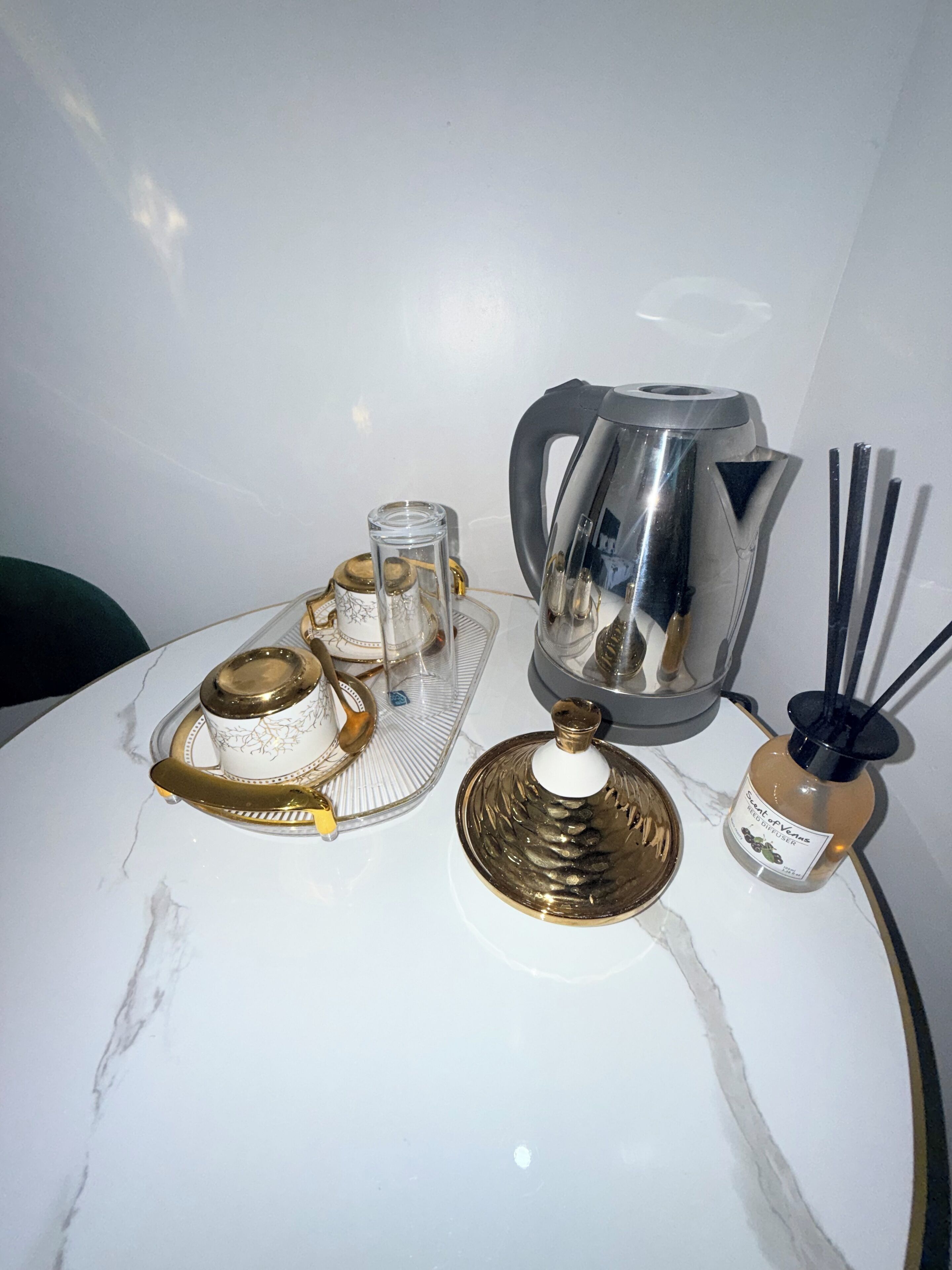 A marble table with a tea set, a glass decanter, a metal pitcher, and a bottle of reed diffuser.