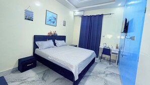 Un dormitorio con cama, escritorio, silla, espejo y televisor.