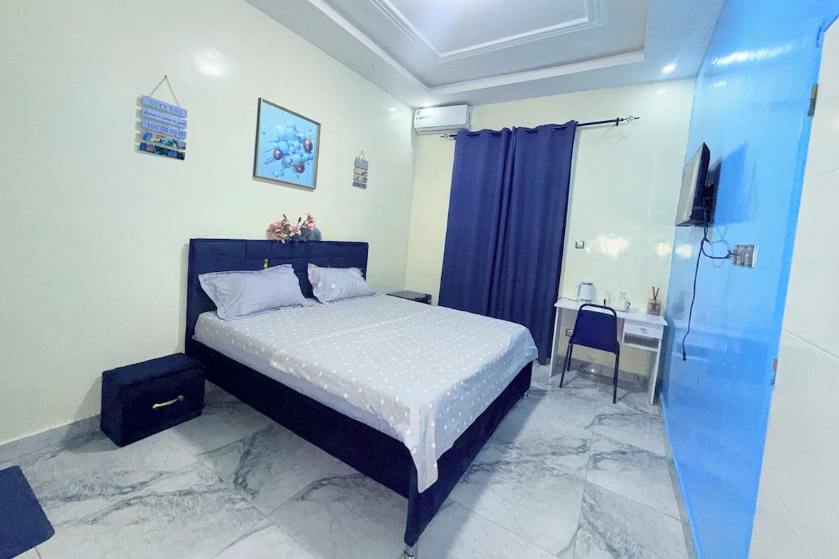 A bedroom with a bed, a desk, a chair, a mirror, and a TV.
