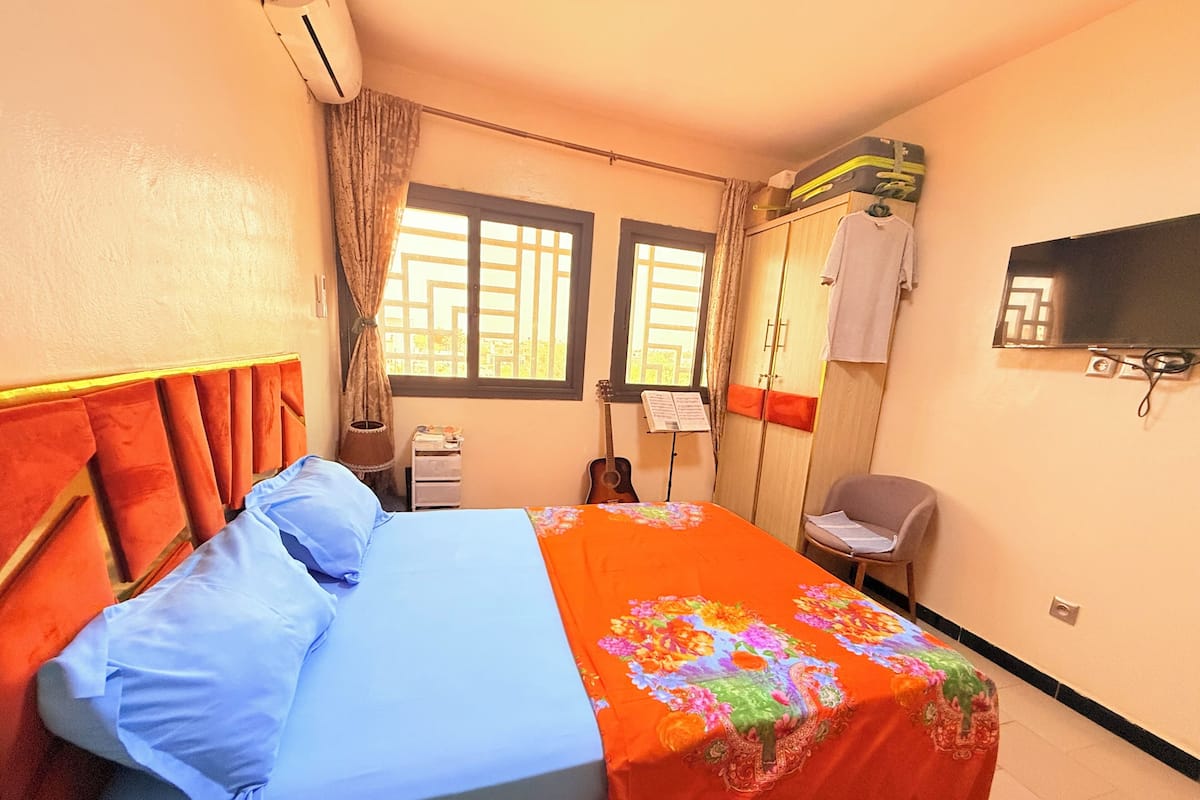 A bedroom with a bed, a chair, a TV, and a window.