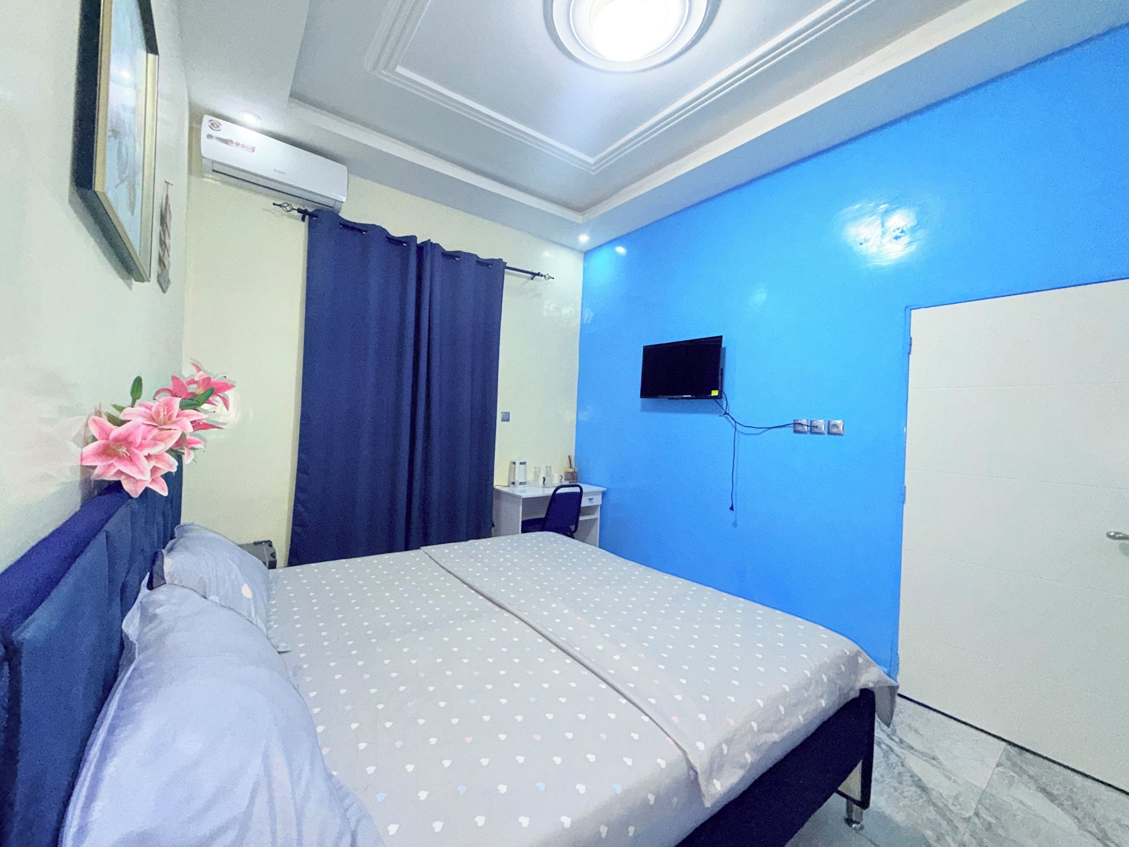 A bedroom with a bed, a TV mounted on the wall, a wardrobe, and a desk with a chair.