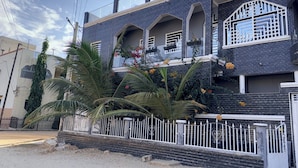 Una casa moderna de dos pisos con balcón, rodeada por una valla blanca y palmeras.