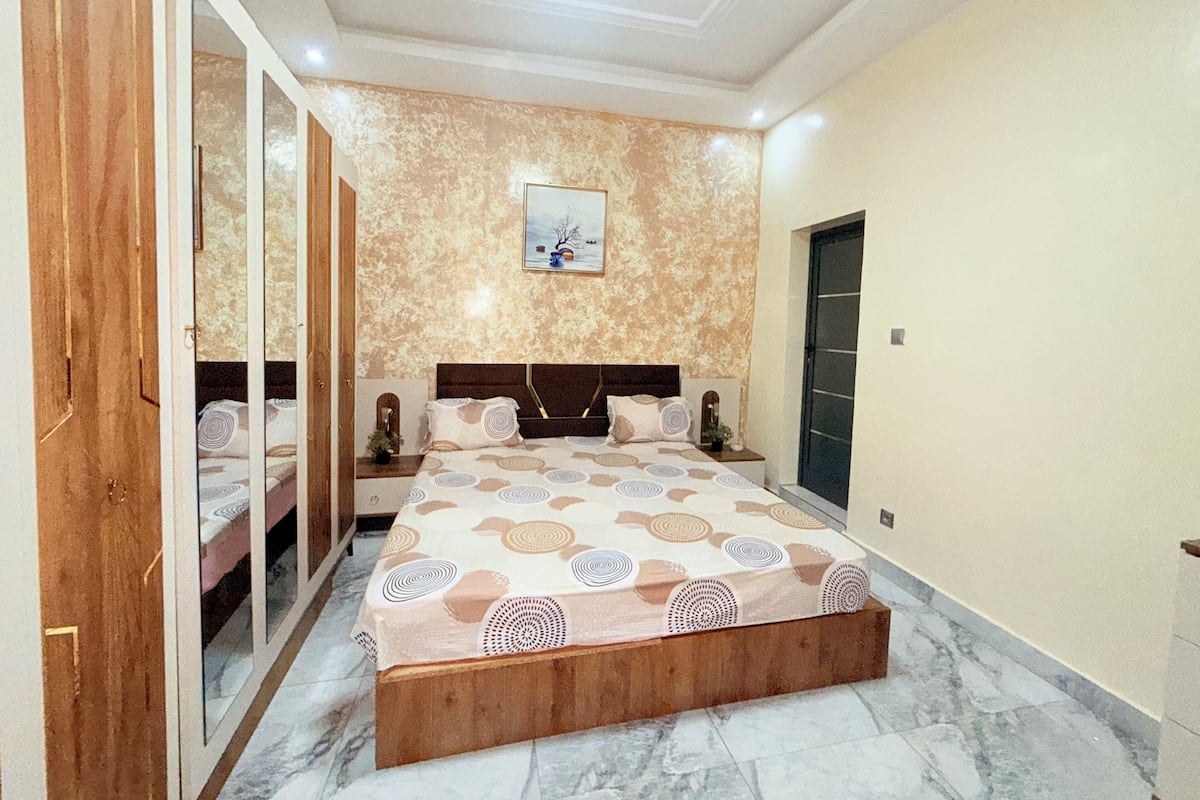A bedroom with a large bed, a wardrobe, a nightstand, and a painting on the wall.