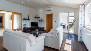 A modern living room with a sofa set, a coffee table, and a flat-screen TV. There is a sliding glass door leading to an outdoor area. - Holiday apartment with air conditioning (Vrsar)