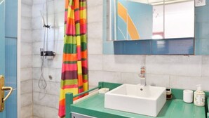 Ein Badezimmer mit Dusche, einem bunten, gestreiften Duschvorhang, einem weißen Waschbecken und einem Spiegel darüber.