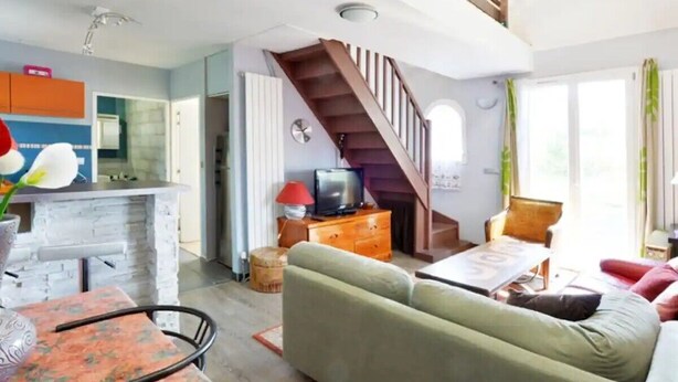 Ein Wohnzimmer mit einer Couch, einem Couchtisch, einem Fernseher und einer Treppe, die zu einer oberen Ebene führt.