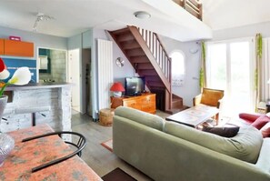 A living room with a sofa, a coffee table, a TV, and a staircase leading to an upper level. - Small house (Férolles-Attilly)