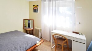 Ein Schlafzimmer mit Bett, Schreibtisch, Stuhl, Heizkörper, Spiegel und einem Fenster mit Vorhängen.