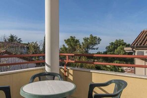 A balcony with a round table and two chairs, a red railing, and a view of trees and buildings. - Holiday apartment with balcony (Dajla)