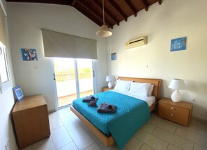 Ein Schlafzimmer mit einem Bett, zwei Nachttischen, einem Fenster und einer Schiebetür zum Balkon.