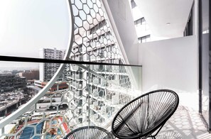 A modern balcony with a geometric metal railing, a black wire chair, and a view of a cityscape with buildings and a sports field. - Free housekeeping visits during your stay - StayShort - Studio in Al Barsha that Sleeps 4 with Premium Building Amenities (Dubai)