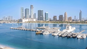 Un port de plaisance où sont amarrés de nombreux yachts, un grand navire blanc et, en arrière-plan, le profil d’une ville avec ses gratte-ciel modernes.