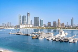 A marina with multiple yachts docked, a large white ship, and a city skyline with modern skyscrapers in the background. - Free housekeeping visits during your stay - StayShort - Beach Front 1 Bed that Sleeps 4 with Amazing Views (Dubai)