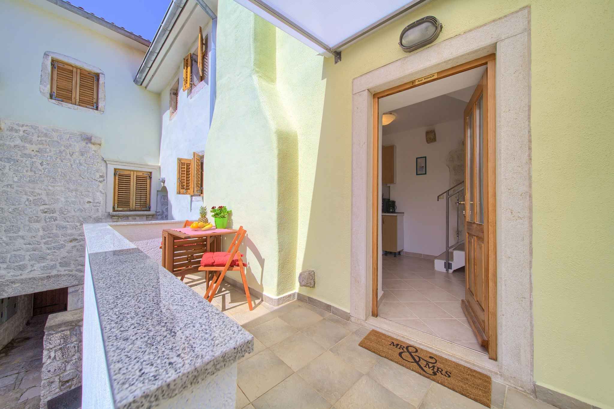 Une petite cour avec un mur en pierre, une table entourée de chaises et une porte donnant sur un espace intérieur.