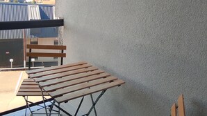 Un balcón con mesa y sillas de madera, vista a edificios distantes y una pared con textura.