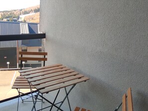 A balcony with a wooden table and chairs, a view of buildings in the distance, and a textured wall. - Modern apartment for 4 in central Super Besse with parking (Besse-et-Saint-Anastaise-Super Besse)