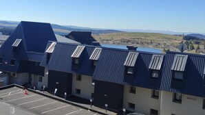 Fila de edificios con techos azules, un estacionamiento al frente y un paisaje montañoso al fondo.