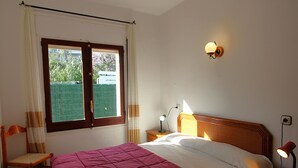 Et soveværelse med seng, stol, natbord, lampe og et vindue med gardiner.