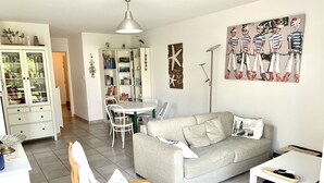 Ett vardagsrum med en grå soffa, en trästol, ett matbord med stolar, en bokhylla och en tavla på väggen.