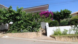 Un barrio residencial con una casa blanca, un muro de piedra y una escalera que lleva a un portón negro.