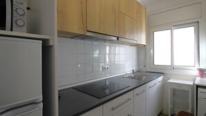 Una cocina con armarios blancos, encimera negra, pileta de acero inoxidable y una ventana con persianas.