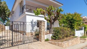Una casa blanca de dos pisos con un pilar de piedra, una reja metálica y un árbol en el jardín delantero.