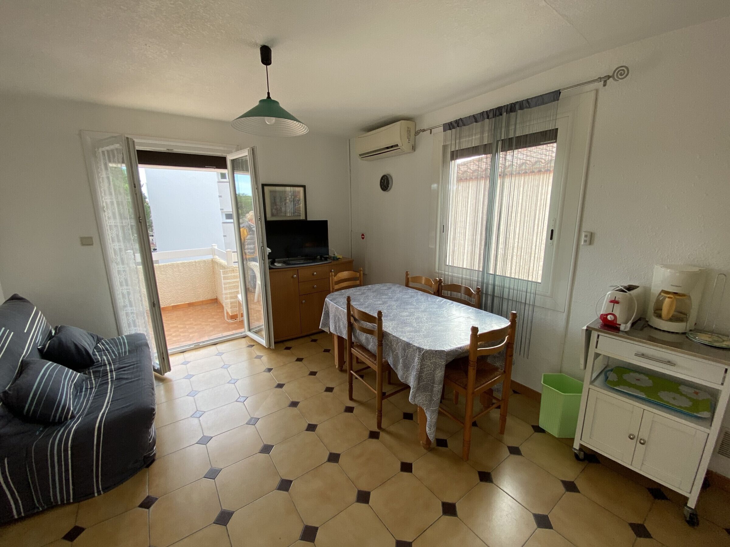 Een compacte woonruimte met een eethoek, een bank, een televisie en een kitchenette.