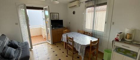 Een compacte woonruimte met een eethoek, een bank, een televisie en een kitchenette.