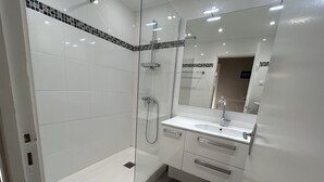 Een moderne badkamer met een douchecabine van glas, een wit wastafeltje en een spiegel.