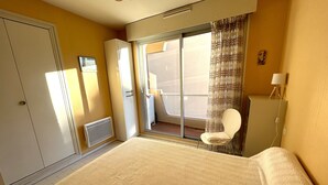 Een hotelkamer met een bed, een stoel, een toilet, een kledingkast en een schuifglazen deur naar buiten.