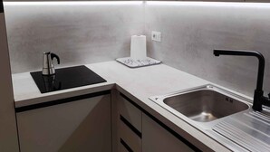 Cozinha moderna com fogão por indução preto, pia de aço inoxidável e bancada branca.