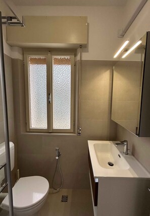 Ein kleines Badezimmer mit Toilette, Waschbecken, Dusche und einem Fenster mit Milchglas.