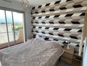 A bedroom with a large bed, a nightstand, a lamp, and a view through a window. - Cozy apartment for 2 in Argelès-sur-Mer, 50m from beach, with parking (Argelès-sur-Mer)