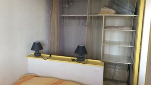 Un dormitorio con cama, dos lámparas de noche, un armario con espacio para colgar y una ventana con cortinas.