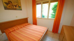 Ein Schlafzimmer mit einem Bett, einem Fenster mit Vorhängen, einem Holzkopfende und einem Gemälde an der Wand.