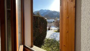 A view from a window with a wooden frame, overlooking a snowy landscape with a building and mountains in the distance.
