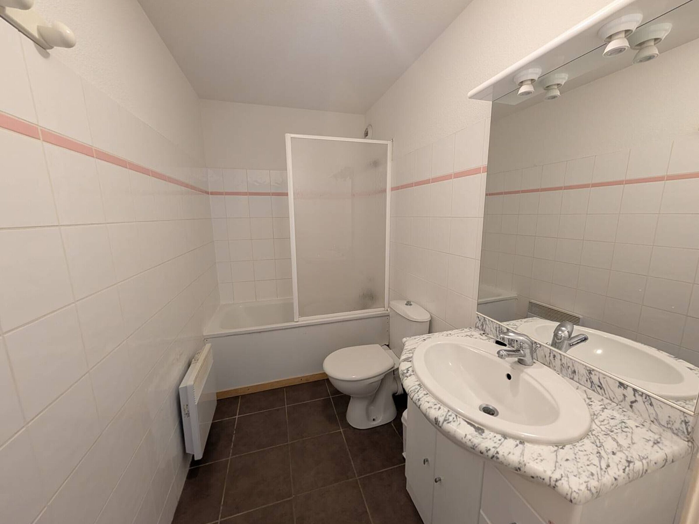 Un bagno con piastrelle bianche, una doccia, un water e un lavabo con piano in marmo.