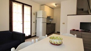 A compact living space with a kitchenette, a dining area with a table and chairs, a sofa, and a television. - Holiday apartment mit Terrasse (Lignano Sabbiadoro)