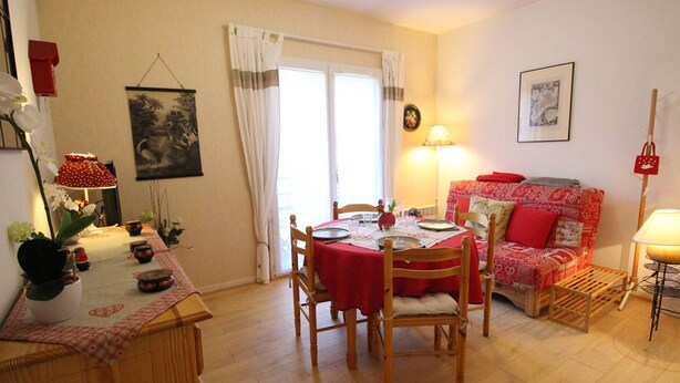 En spiseplads med et bord dækket til to personer, en rød sofa og en lampe.