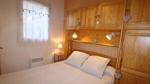 Et soveværelse med sengegavl i træ, to sengeborde med lamper, et vindue med gardiner og et natbord med lampe.