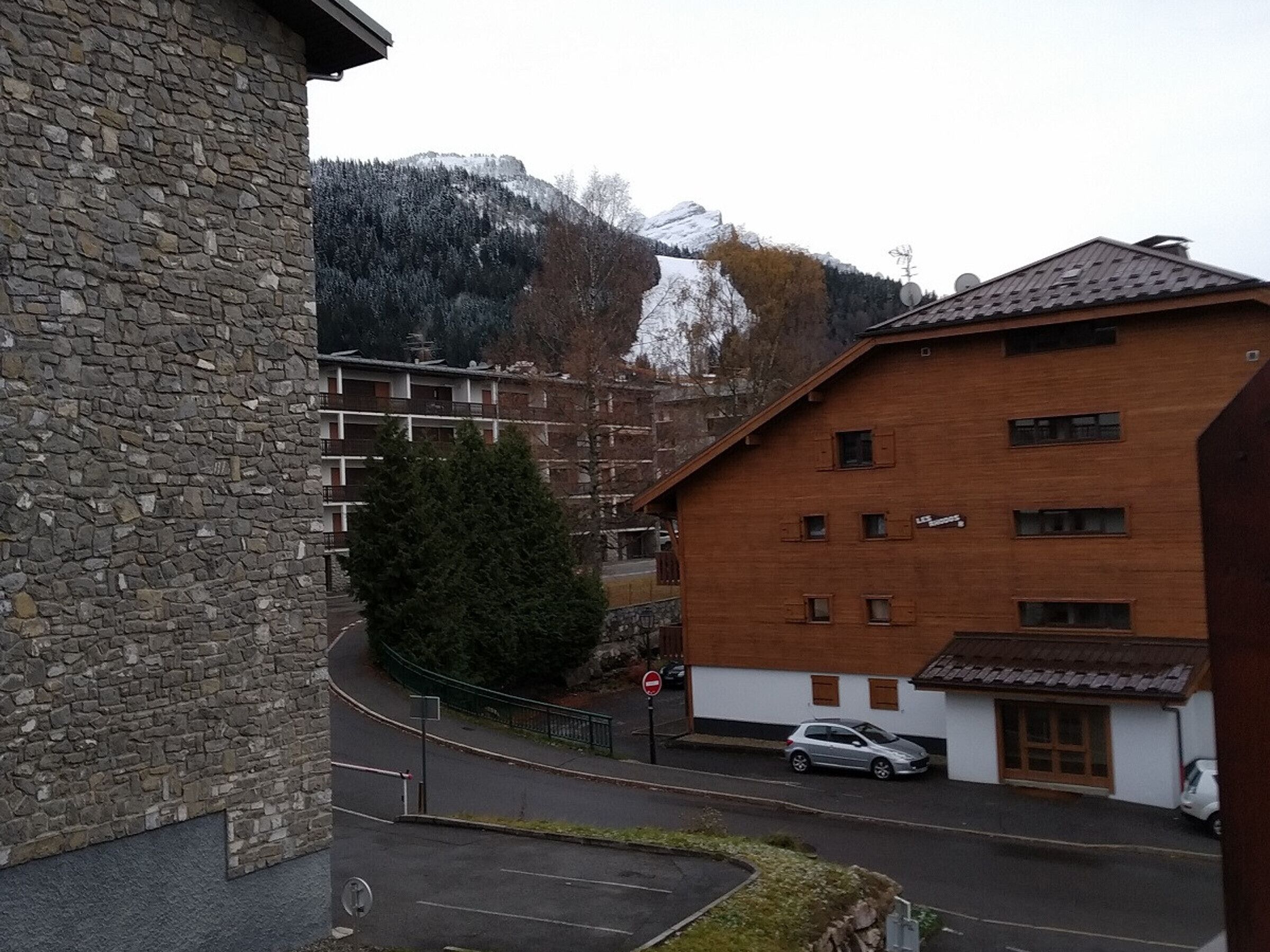A stone building with a modern brick structure in the background, a parked car, and a mountain in the distance.