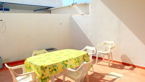 Eine Terrasse mit Tisch und Stühlen, eine weiße Wand und ein gefliestes Podest.
