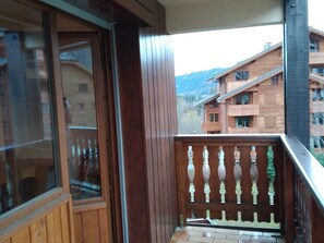 Ein Holzbalkon mit Glastür und Blick auf ein mehrstöckiges Gebäude mit Balkonen.