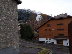 A stone building with a modern brick structure in the background, a parked car, and a mountain in the distance. - Studio 4 pers Central - Pets Allowed (Arâches-la-Frasse)