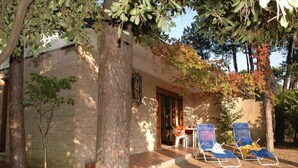 A building with a brick exterior, a wooden door, and a small porch with two blue lounge chairs and a table. - Holiday apartment mit Terrasse (Lignano Sabbiadoro)