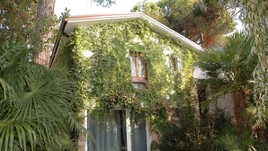 A house with a covered patio area, surrounded by lush greenery and palm trees. - Holiday apartment mit Terrasse (Lignano Sabbiadoro)