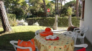 An outdoor dining area with a table set for four, surrounded by white plastic chairs. - Holiday apartment mit Garten (Lignano Sabbiadoro)